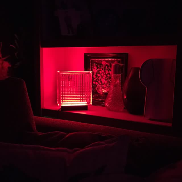 Lamp glowing red on a living-room shelf beside a framed print and glass decanter